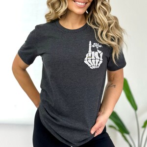Pode incluir: Uma camiseta cinza escura com uma m&atilde;o de esqueleto branca usando um anel. O texto "Mrs." est&aacute; impresso na camiseta.