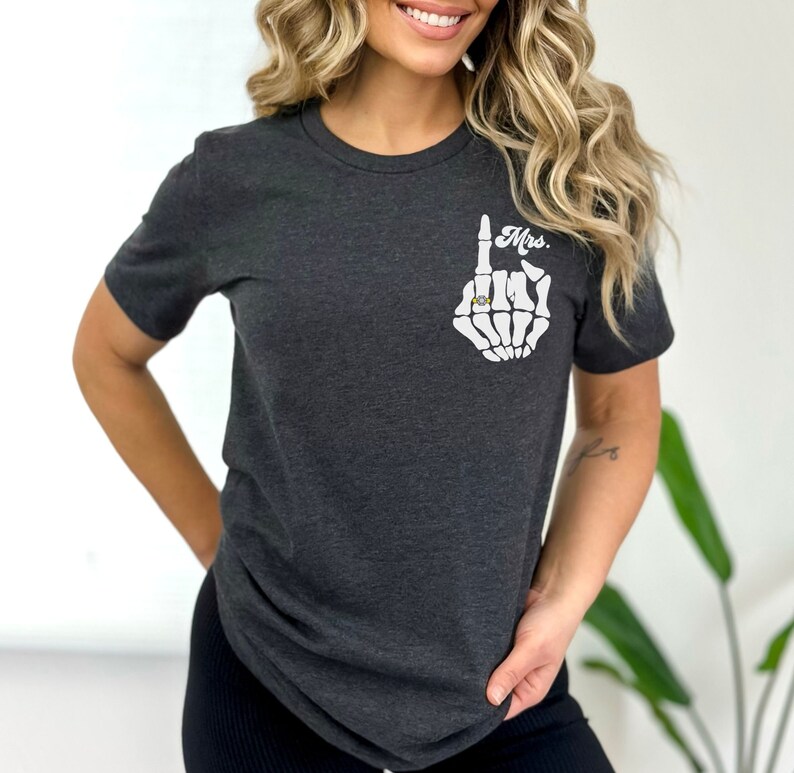 Pode incluir: Uma camiseta cinza escura com uma m&atilde;o de esqueleto branca usando um anel. O texto "Mrs." est&aacute; impresso na camiseta.