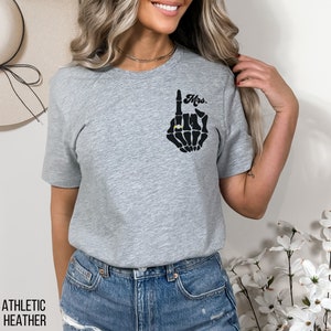 Pode incluir: Camiseta cinza com uma m&atilde;o de esqueleto preto usando um anel. A m&atilde;o est&aacute; fazendo um gesto de "um" e o texto "Mrs." est&aacute; acima da m&atilde;o.