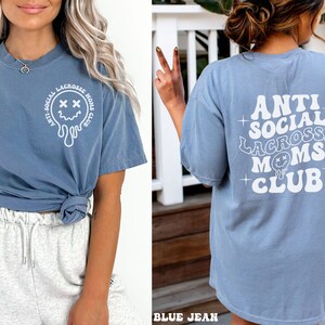 May include: A blue t-shirt with a white graphic that says "Anti-Social Lacrosse Moms Club" and a dripping smiley face with X's for eyes.