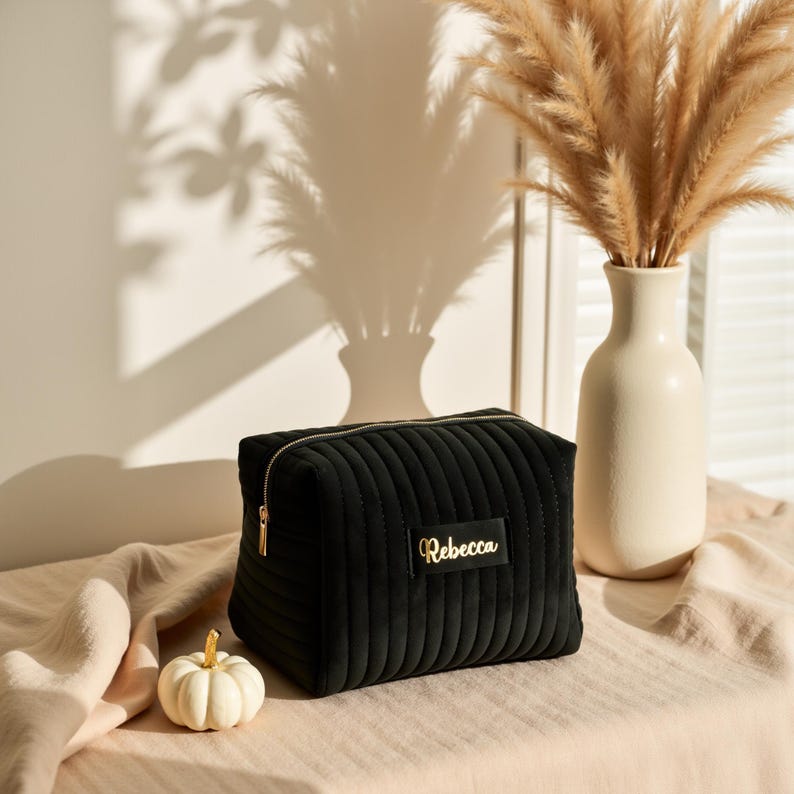 a black bag sitting on top of a bed next to a vase