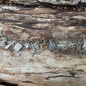 May include: A silver charm bracelet with a variety of charms, including a dice, a horseshoe, a sailboat, a bird, and a heart. The bracelet is on a wooden surface.