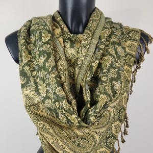 Peut inclure: Écharpe à motif cachemire vert et beige, avec une bordure décorative et des franges. L'écharpe est drapée sur un mannequin noir, mettant en valeur le motif complexe et la palette de couleurs. Les dimensions de l'écharpe ne sont pas visibles.