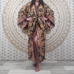 Peut inclure: Une longue robe noire et dorée à motifs avec des accents roses. La robe a un col large et des manches longues. Elle est nouée à la taille avec une ceinture assortie.