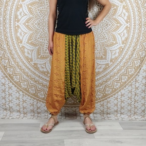 Peut inclure: Pantalon de style harem jaune moutarde avec un motif géométrique et un panneau vert à motifs au centre. Le pantalon a des poignets élastiques aux chevilles. La personne porte un débardeur noir et des sandales beiges.