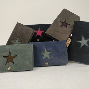 Può includere: Una collezione di portafogli in camoscio in vari colori, tra cui grigio, blu e nero. Ogni portafoglio presenta un ritaglio a forma di stella con un inserto a contrasto e una chiusura a scatto. I portafogli misurano circa 18 cm di lunghezza.