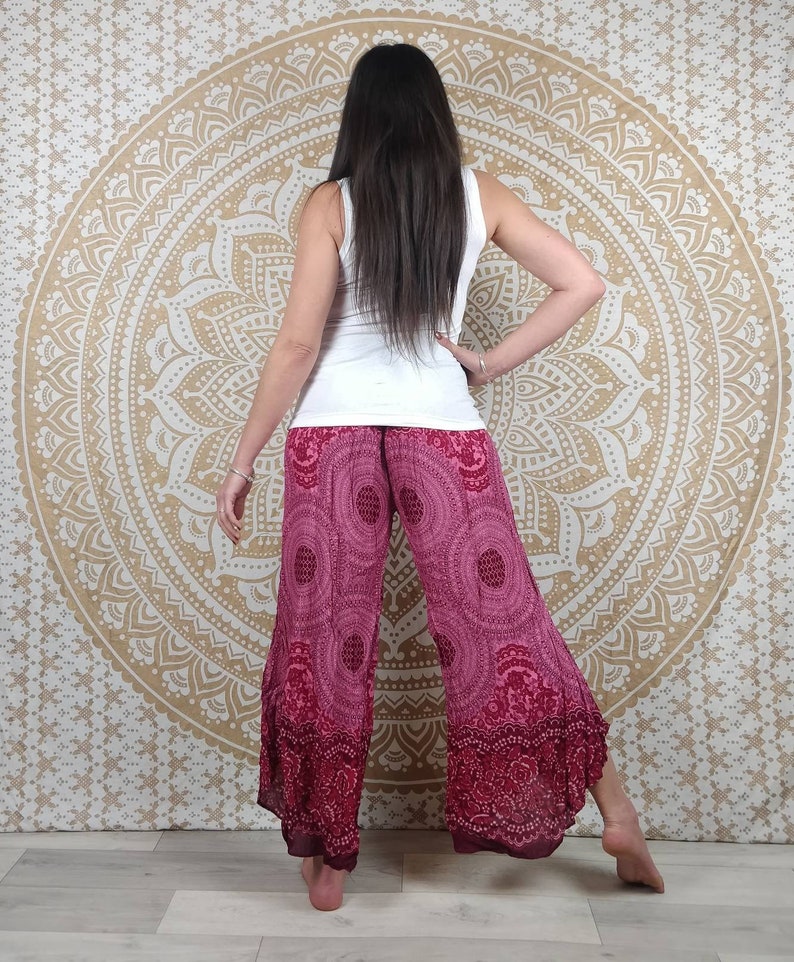 Puede incluir: Una persona con una camiseta sin mangas blanca y pantalones anchos magenta con un patr&oacute;n circular. Los pantalones tienen un borde magenta m&aacute;s oscuro. El fondo es un tapiz de mandala dorado.