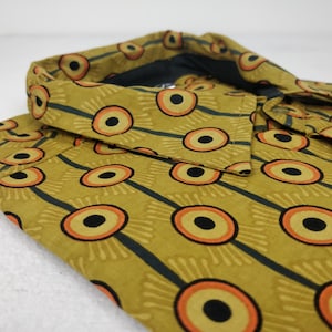 Könnte beinhalten: Ein gelbes, orangefarbenes und schwarzes Hemd mit Kragen. Das Muster zeigt ein sich wiederholendes Design aus stilisierten Augen.