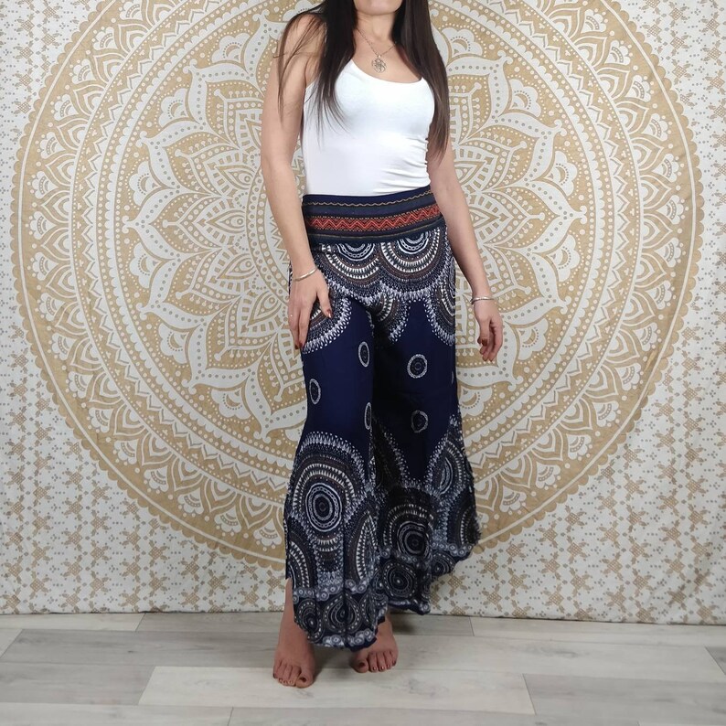 Puede incluir: Pantalones palazzo azul marino con un estampado circular blanco y gris. Los pantalones tienen una cintura ancha con un dise&ntilde;o rojo y naranja. La modelo lleva una camiseta sin mangas blanca. El fondo es un dise&ntilde;o de mandala dorado.