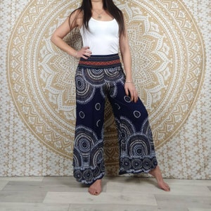 Puede incluir: Pantalones palazzo azul marino con un estampado circular blanco y marr&oacute;n. Los pantalones tienen una cintura ancha con un dise&ntilde;o geom&eacute;trico rojo y naranja. La modelo lleva una camiseta sin mangas blanca. El fondo es un tapiz dorado con un dise&ntilde;o circular.