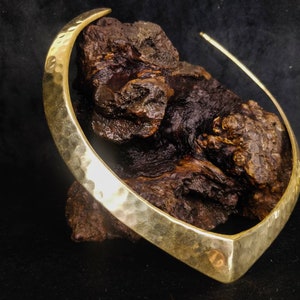 Puede incluir: Un collar gargantilla de metal martillado dorado con un frente puntiagudo. El collar se muestra sobre una pieza de madera marrón oscura.