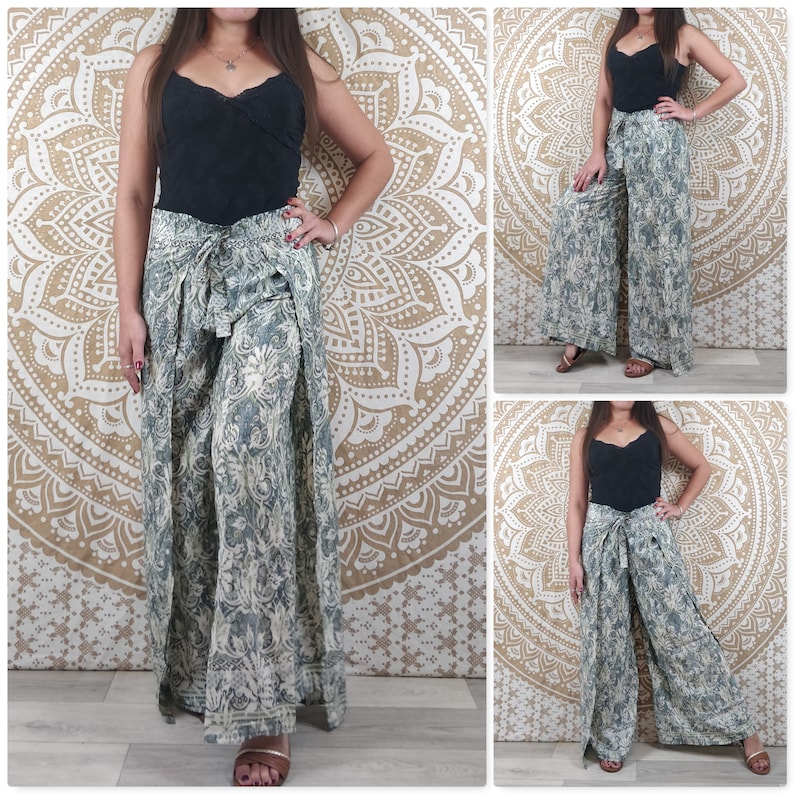 Op de afbeelding: Een wijde broek met een bloemenprint in tinten van groen en wit. De broek heeft een strik in de taille en een split aan elke kant. De broek wordt getoond op een model dat een zwart tanktop draagt.