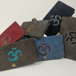 Könnte beinhalten: Sechs verschiedene farbige Stoffgeldbörsen mit einem gestickten Om-Symbol in verschiedenen Farben. Die Geldbörsen sind aus einem weichen, strukturierten Stoff gefertigt und haben ein schlichtes, minimalistisches Design.