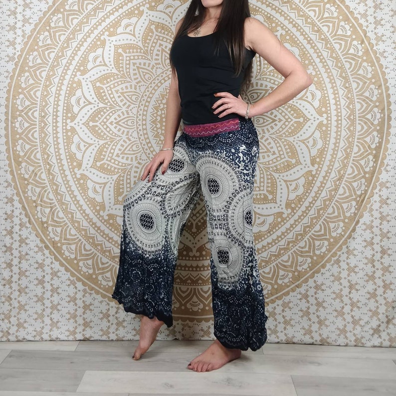 Puede incluir: Pantalones de pierna ancha con un estampado circular en azul marino y blanco. Los pantalones tienen un dobladillo azul oscuro y una cintura rosa. La modelo lleva una camiseta sin mangas negra. El fondo es un tapiz mandala dorado.