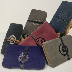 May include: Six different suede pouches with a circular design and a tie closure. The pouches are in various colours, including brown, red, black, blue, and grey.
