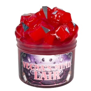 Puede incluir: Un tarro de slime rojo cubierto con cubos rojos y detalles plateados. El tarro tiene una etiqueta con el texto "VECNA'S MIND LAIR" en rosa y blanco, sobre un fondo morado y negro.