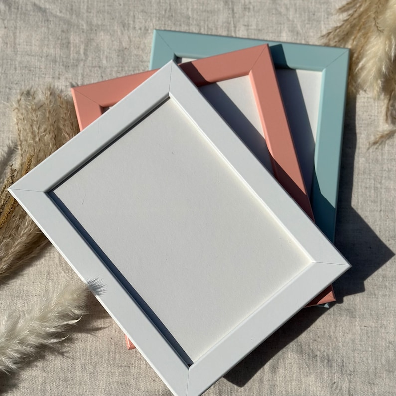 May include: Three picture frames stacked on top of each other. The top frame is light blue, the middle frame is pink, and the bottom frame is white.