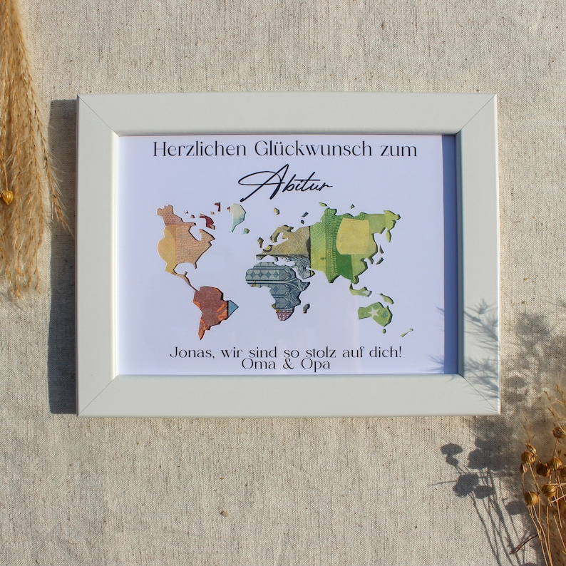 May include: A white framed picture with a world map made of money. The text "Herzlichen Gl&uuml;ckwunsch zum Abitur" is at the top of the picture. The text "Jonas, wir sind so stolz auf dich! Oma & Opa" is at the bottom of the picture.