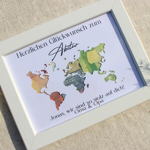 May include: A white framed picture with a world map made of money. The text "Herzlichen Gl&uuml;ckwunsch zum Abitur" is at the top of the picture. The text "Jonas, wir sind so stolz auf dich! Oma & Opa" is at the bottom of the picture.