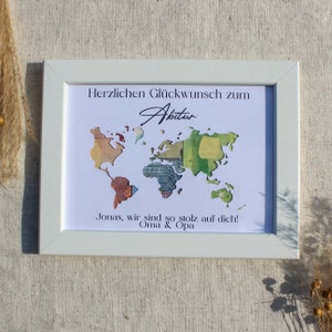 May include: A white framed picture with a world map made of money. The text "Herzlichen Gl&uuml;ckwunsch zum Abitur" and "Jonas, wir sind so stolz auf dich! Oma & Opa" is printed on the picture.