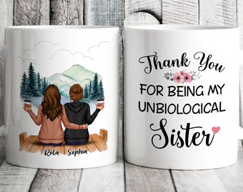 May include: Two white coffee mugs with a design of two women sitting on a dock overlooking a lake and mountains. One mug says "Thank You For Being My Unbiological Sister" with a pink heart. The other mug has the names "Rolla" and "Sophia" written on the bottom.