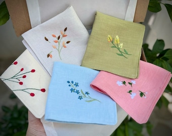 May include: Five embroidered handkerchiefs with different floral designs. The handkerchiefs are in shades of white, light blue, light green, pink, and beige.