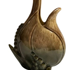 May include: A ceramic vase shaped like a stylized flower with a green and brown glaze. The vase has a wide opening and a narrow neck.