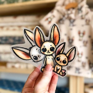Op de afbeelding: Drie transparante vinyl stickers met cartoon illustraties van fennekvossen. De vossen zijn getekend in een grillige stijl met grote ogen en oren. De stickers zijn perfect om een ​​toetsje schattigheid toe te voegen aan laptops, waterflessen of dagboeken.