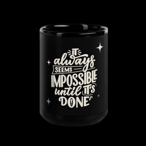 Könnte beinhalten: Schwarze Keramik-Tasse mit dem Zitat "It always seems impossible until it's done" in weißer Schrift. Die Tasse hat eine zylindrische Form und ist mit Sternen verziert. Das Design ist zentriert.