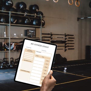 Könnte beinhalten: Ein Tablet mit einer Vorlage für Fitnessziele wird in einem Fitnessstudio gehalten. Die Vorlage enthält Abschnitte für Fitnessziele, Gewohnheiten zum Streichen und Beibehalten sowie Körpermaße. Der Text "MY FITNESS GOALS" ist oben sichtbar.