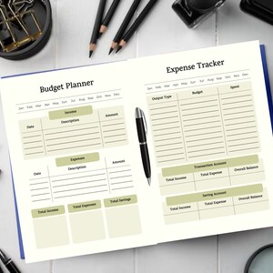Könnte beinhalten: Offenes cremefarbenes Notizbuch mit Budgetplaner und Ausgaben-Tracker. Die Seiten haben einen blauen Rand. Der Planer enthält Abschnitte für Einnahmen, Ausgaben und Ersparnisse. Ein Stift liegt auf der rechten Seite.
