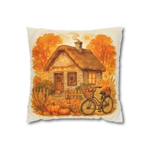 Könnte beinhalten: Ein dekoratives Kissen mit einer Aquarellillustration einer herbstlichen Cottage-Szene. Das Bild zeigt ein Haus mit Strohdach, Kürbisse, ein Fahrrad mit Obstkörben und orangefarbenes und gelbes Herbstlaub.