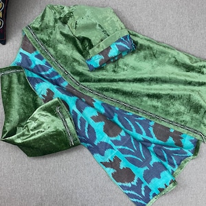 May include: Green velvet garment with a contrasting blue and teal patterned fabric. The garment has long sleeves and a decorative trim. The fabric has a soft, textured appearance. The item is likely a piece of clothing.