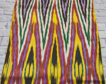 May include: A colorful fabric with a repeating pattern of yellow, green, black, white, and brown. The pattern is a chevron design with a diamond shape in the center of each chevron.