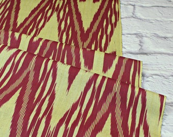 Può includere: Tessuto ikat rosso e giallo con un motivo a righe. Il tessuto è piegato e ha una superficie testurizzata.