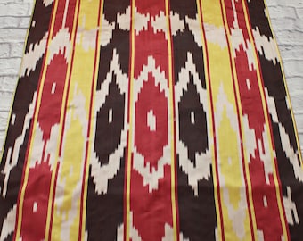 Può includere: Tessuto a righe con un motivo ripetuto di rosso, giallo, bianco e nero. Il tessuto ha una trama tessuta e un design ikat tradizionale.