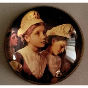 May include: A vintage glass paperweight featuring a painting of three young girls wearing white bonnets. The girls are dressed in simple clothing and have serious expressions on their faces. The paperweight has a dark brown rim.