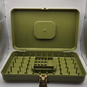 May include: Open olive green sewing box with a hinged lid and a gold-coloured clasp. The interior features multiple pegs for thread spools and a small compartment for notions. The box is empty and ready for use.