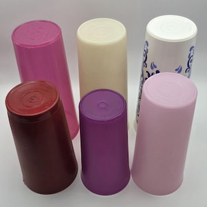 Puede incluir: Colección de seis vasos de plástico en varios colores, incluyendo rosa, burdeos, morado y crema. Un vaso presenta una base blanca con un diseño floral azul. Los vasos son cilíndricos con tapas del mismo color.