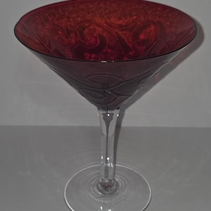 Könnte beinhalten: Ein rubinrotes Martini-Glas mit klarem Stiel und Fuß. Die Schale des Glases hat ein geätztes, wirbelndes Design. Das Glas besteht aus klarem Glas und eignet sich für Cocktails.