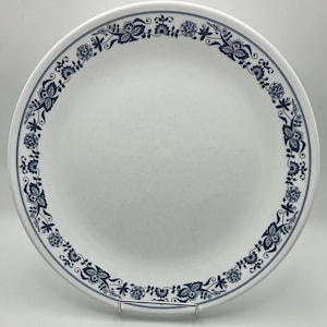 Może przedstawiać: Biały ceramiczny talerz z granatowym wzorem kwiatowym. Talerz ma delikatny wzór kwiatów i liści na obrzeżu. Ten dekoracyjny talerz nadaje się do serwowania posiłków lub jako element dekoracyjny.