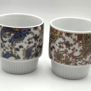 Könnte beinhalten: Ein Set aus drei Keramikbechern mit gesprenkelter, matter Oberfläche. Jeder Becher hat eine andere Farbe: hellblau, creme und grau. Die Becher haben ein schlichtes, modernes Design mit runder Form und bequemem Griff.
