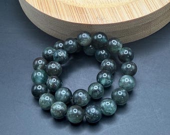 May include: A dark green beaded bracelet with a polished finish. The bracelet is made of round beads and is displayed on a black surface. The beads have a speckled appearance and are arranged in a circular pattern.