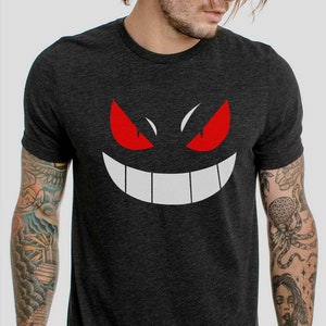 Könnte beinhalten: Ein dunkelgraues T-Shirt mit einer weißen und roten Grafik eines Geistergesichts. Der Geist hat rote Augen und ein breites weißes Lächeln.