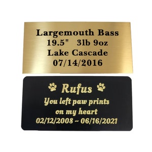 May include: Gold and black pet memorial plaque with the text "Largemouth Bass 19.5" 3lb 9oz Lake Cascade 07/14/2016" and "Rufus You left paw prints on my heart 02/12/2008 - 06/16/2021"
