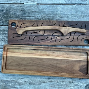 May include: A wooden cutting board with a built-in knife. The board is made of walnut wood and has a natural finish. The knife is made of wood and has a curved blade.