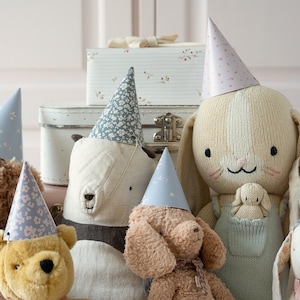 May include: A group of stuffed animals wearing party hats. The animals include a brown bear, a white bunny, a brown dog, and a beige bunny. The hats are blue and white with a floral pattern.