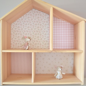 May include: A light-coloured wooden dollhouse with two levels and four rooms. The interior walls feature patterned wallpaper in floral, pink gingham, and striped designs. Two small plush mouse figures are positioned inside the rooms.