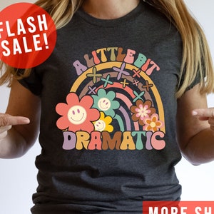 May include: A dark gray t-shirt with a rainbow and flowers graphic. The text "A Little Bit Dramatic" is printed on the shirt.