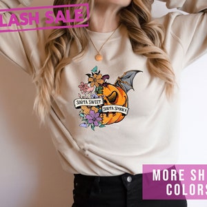 May include: Beige sweatshirt with a pumpkin graphic. The pumpkin is half orange and half floral, with a bat wing and the text "Sorta Sweet Sorta Spooky". A pink "Flash Sale" banner is at the top.